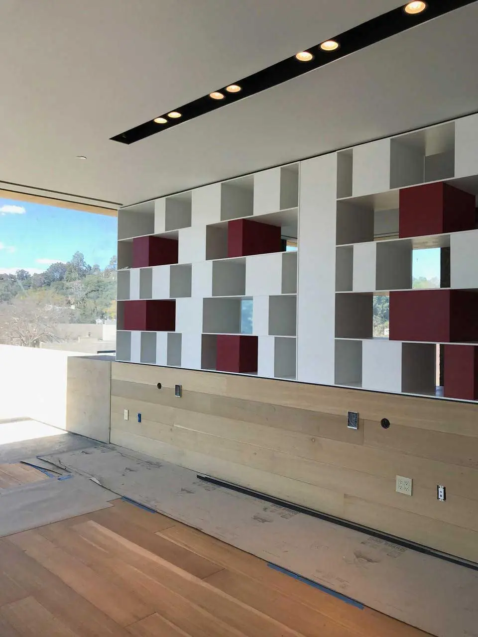 Built-in shelving unit with white and burgundy cubes above a wood-paneled cabinet, under construction