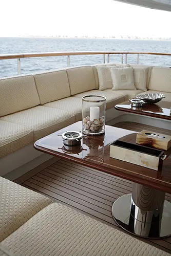 Yacht deck seating area with cream cushions, a wood table and a lit candle