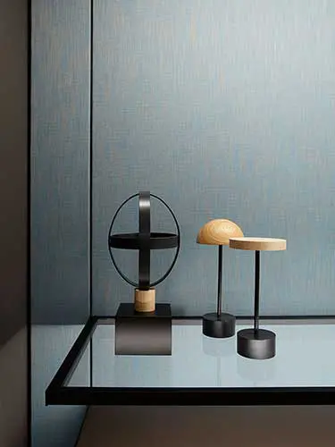 Sculptural black and wood tabletop objects displayed on a glass shelf against a blue wall