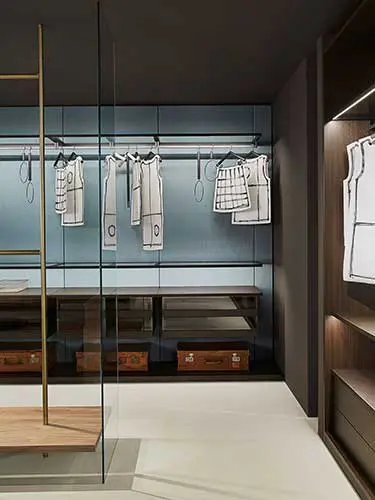 Walk-in closet with a glass partition, garment sketches on hangers and leather suitcases