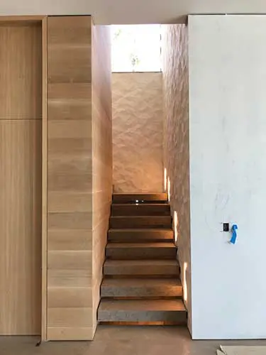 Narrow staircase lit from above between wood paneling and a textured stone wall
