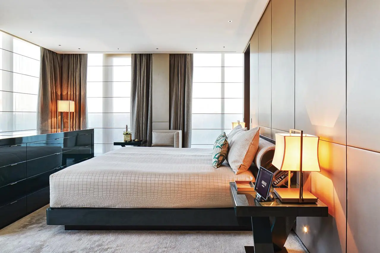 Hotel bedroom with a glossy black dresser and warm bedside lamps by floor-to-ceiling windows