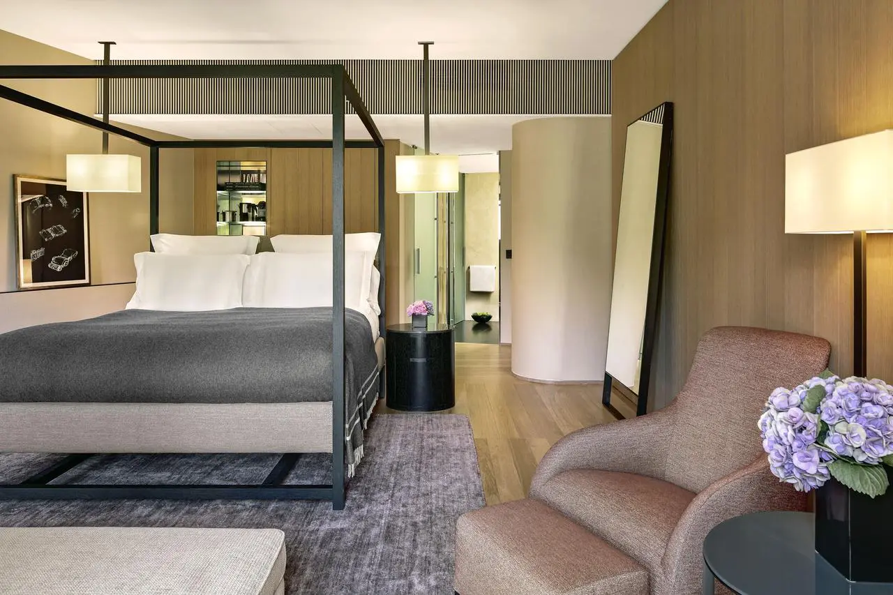 Hotel bedroom with a black four-poster bed frame and a pink upholstered armchair