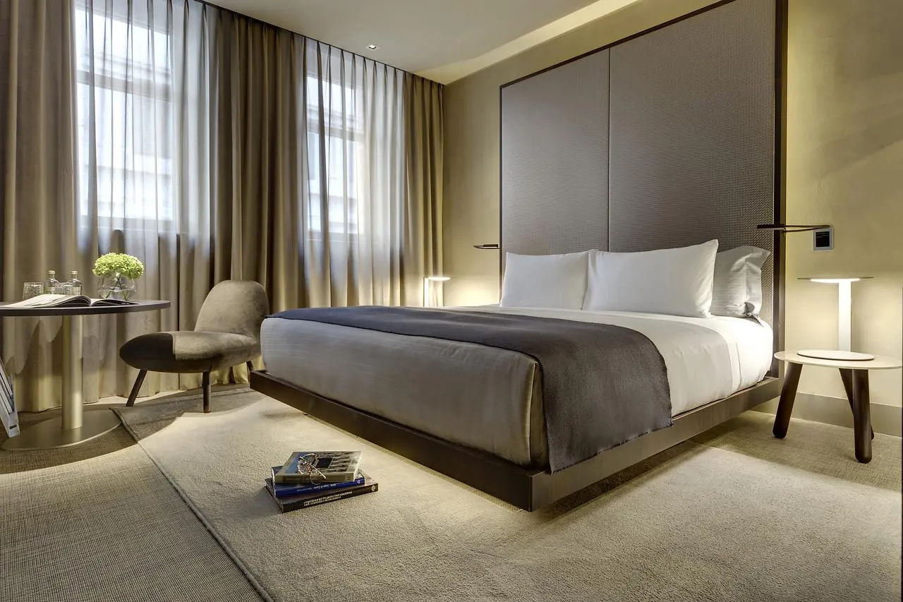 Hotel bed with grey and orange cushions against a tall upholstered headboard