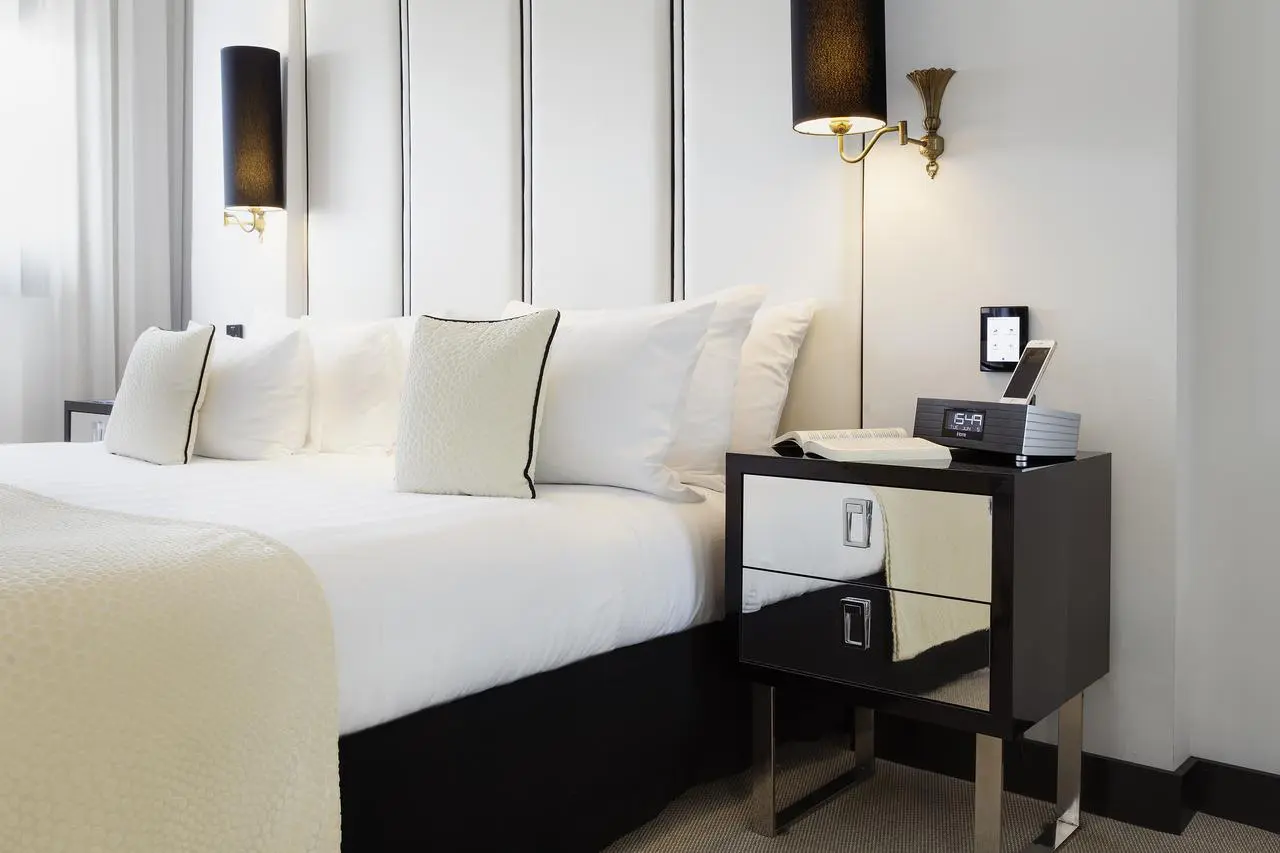 Hotel bed with pillows beside a mirrored nightstand and wall sconce lighting