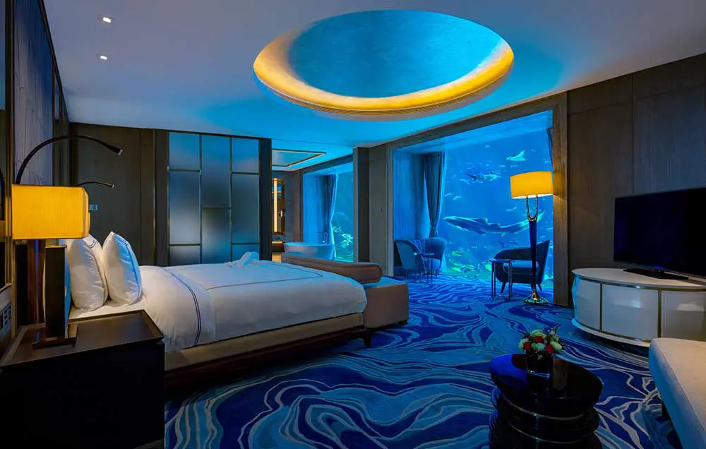 Hotel bedroom with a glowing round ceiling and a floor-to-ceiling aquarium window