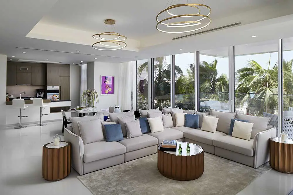 Bright living room with glass walls, palm view, a sectional sofa and round drum tables