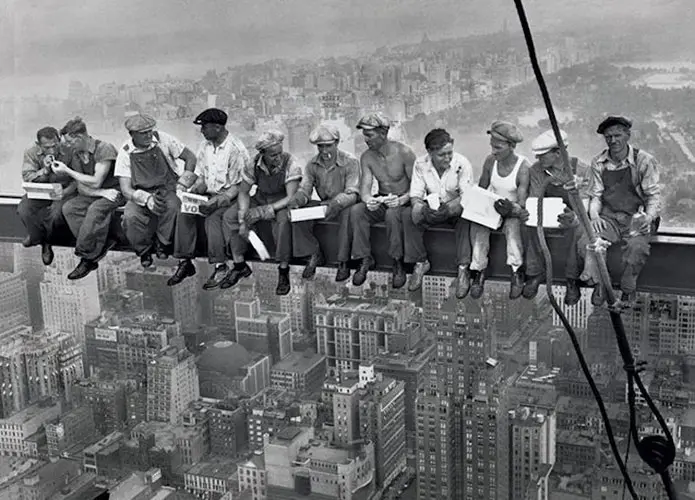 Black and white photo of ironworkers eating lunch on a steel beam high above a city