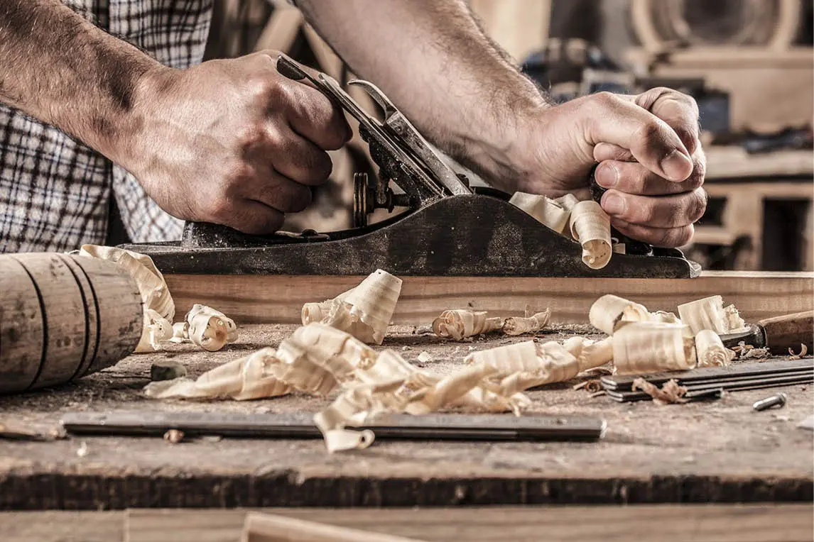 Craftsman planing a wooden board, with wood shavings on the workbench