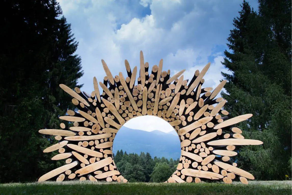 Sculpture of radiating wooden logs framing a view of mountains and forest