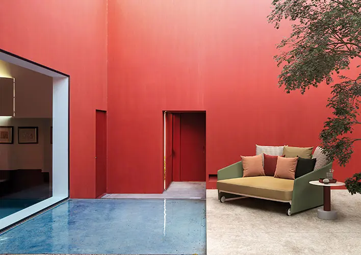 courtyard with a red wall, a doorway and a green and gold outdoor sofa