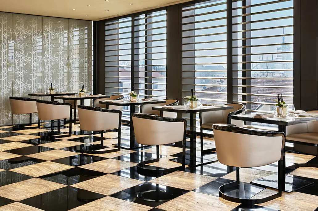 Restaurant with beige armchairs, a checkerboard marble floor and slatted blinds