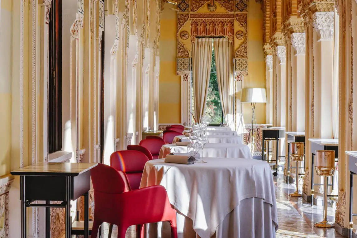 Restaurant hall with red chairs and white tablecloths under gilded decorations
