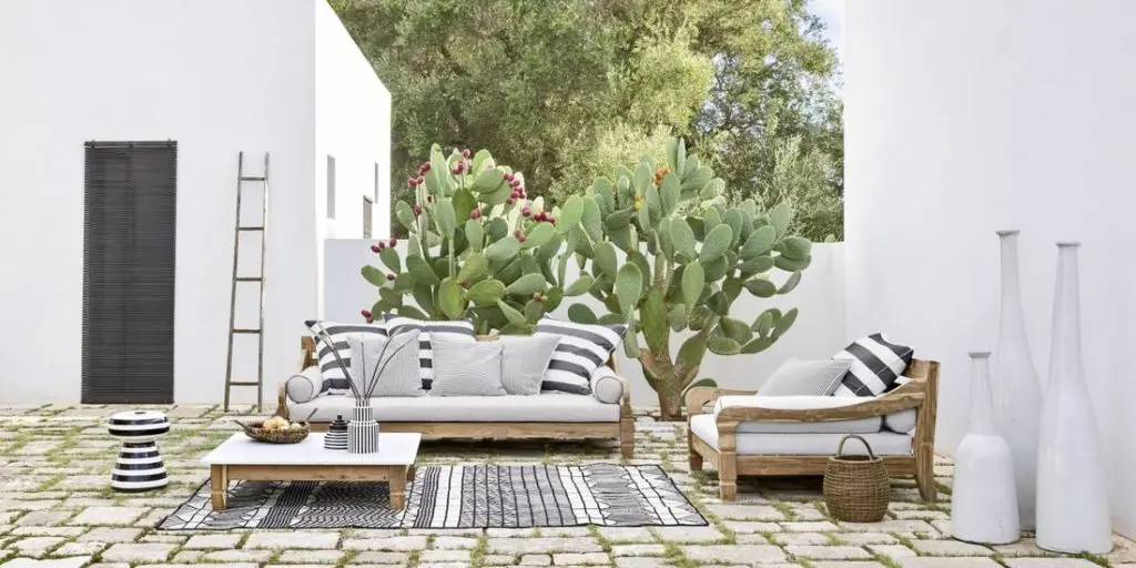Gervasoni Jeko wood-framed sofa and armchair with striped cushions on a stone patio with cacti