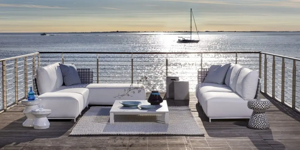 Gervasoni white sectional sofas on a wooden deck overlooking the sea with a sailboat