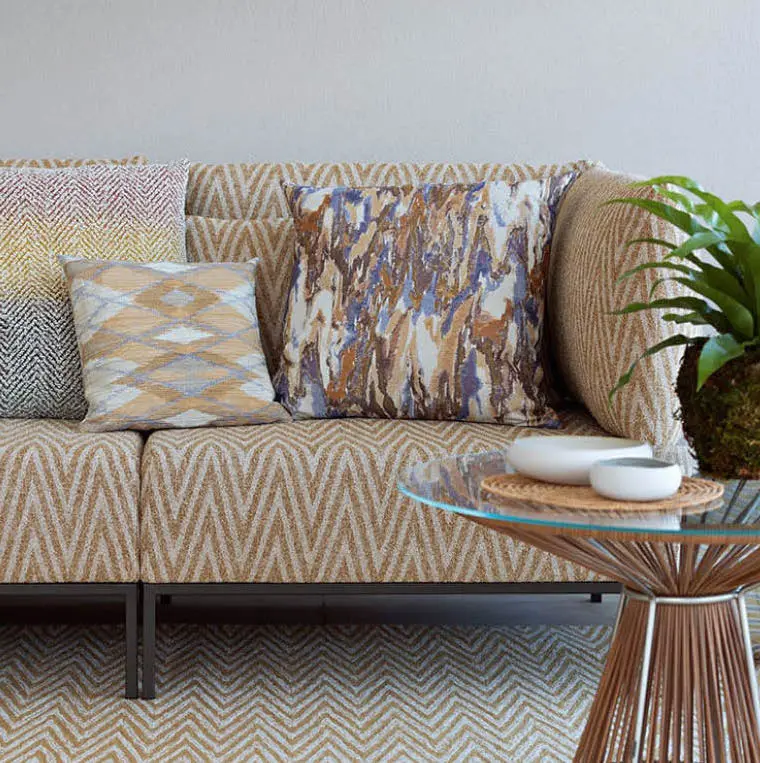 Sofa with patterned cushions next to a glass side table and a plant