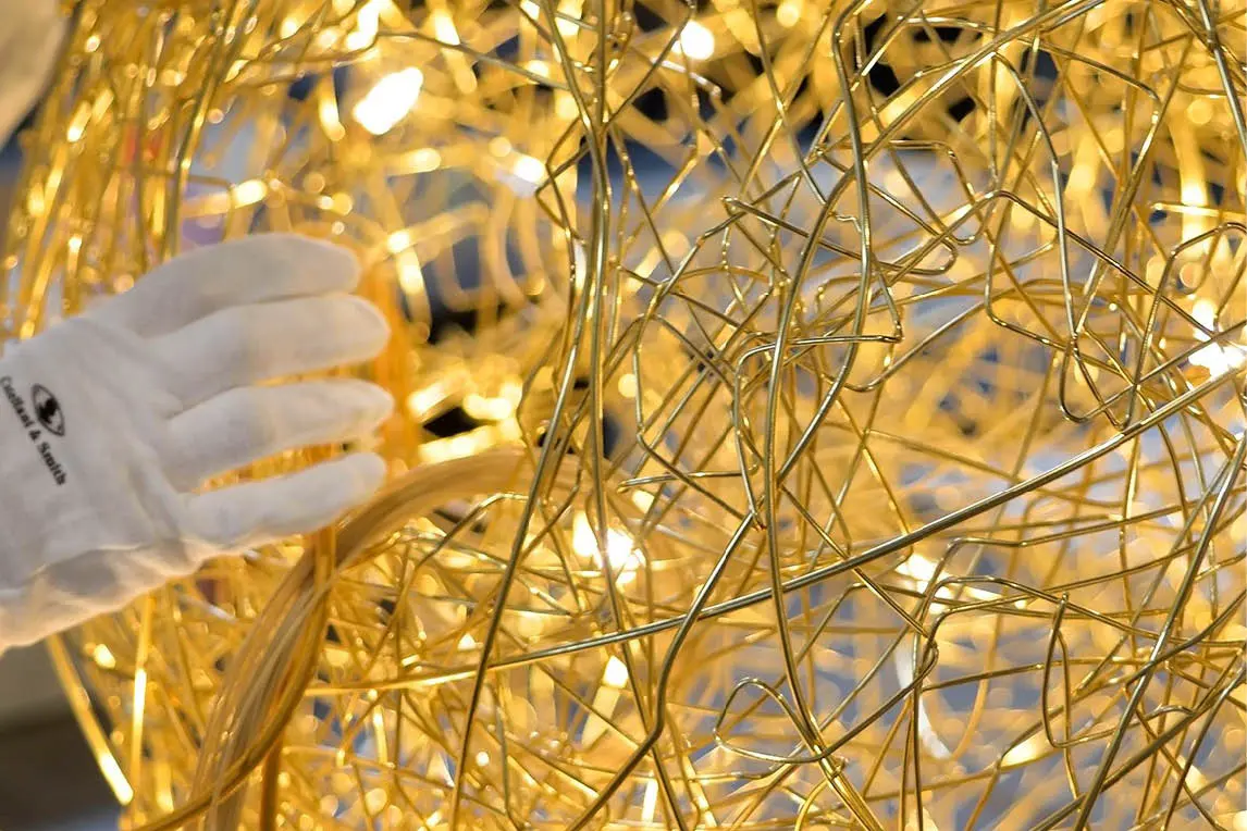 Gloved hand handling a gold wire lighting fixture