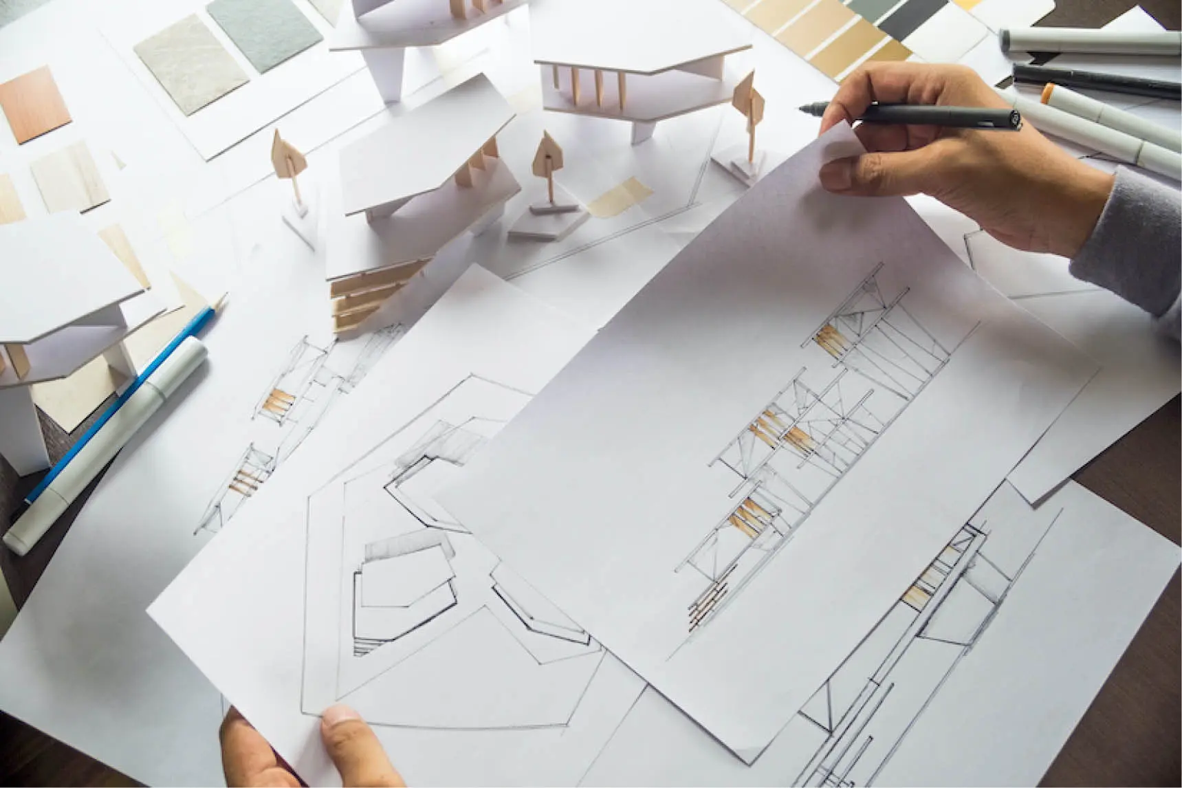 Architect sketching floor plans next to a white architectural model and material samples