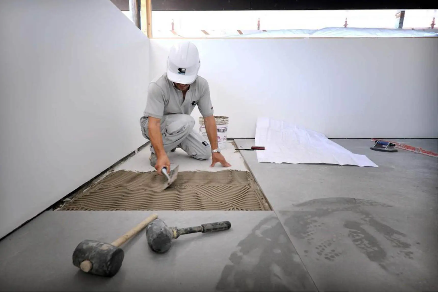 Worker laying large floor tiles, with rubber mallets in the foreground