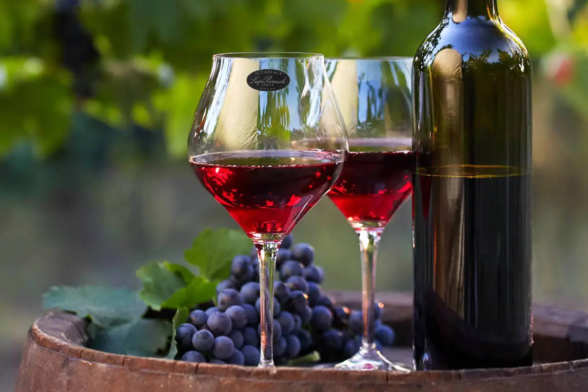 Two glasses of red wine, a bottle and grapes on a barrel