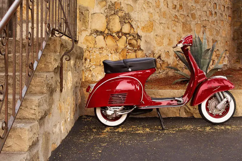 Red scooter parked by a stone wall