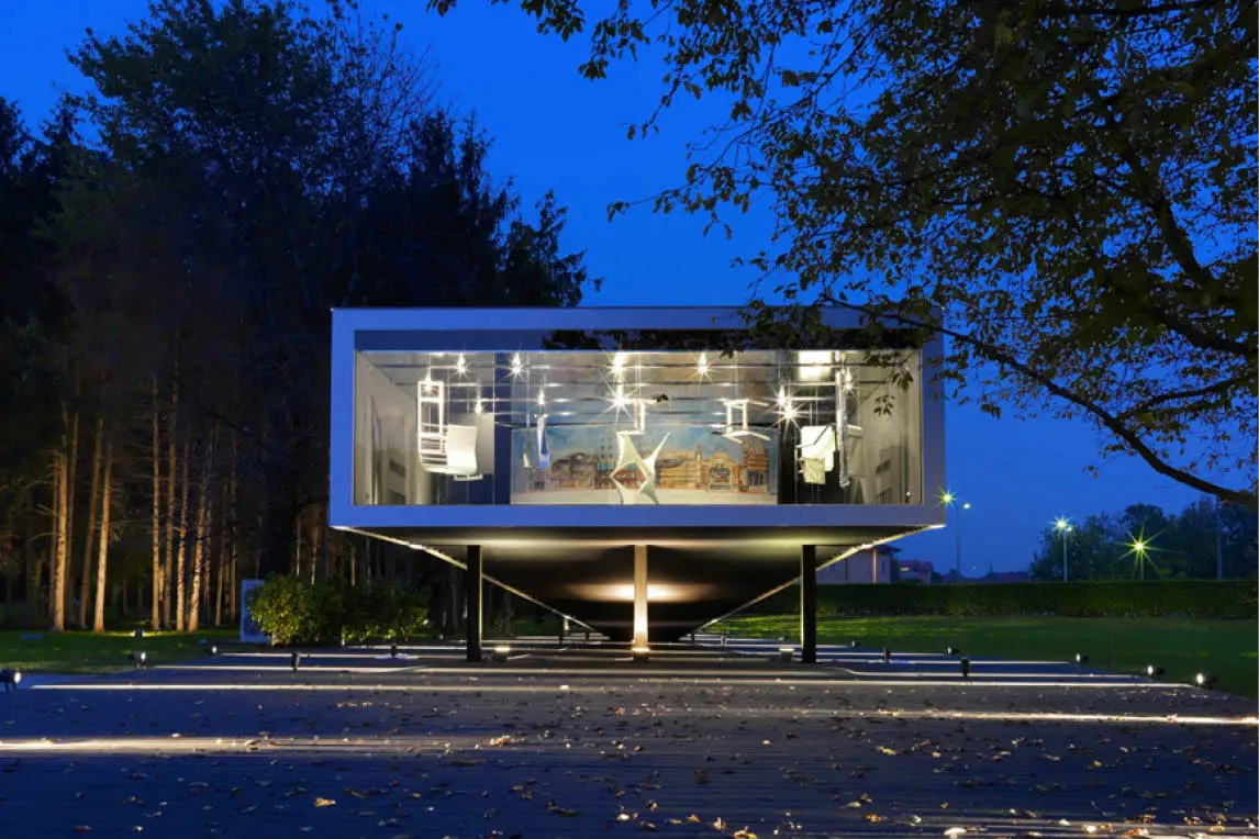 Glass pavilion raised on pillars, lit at night among trees