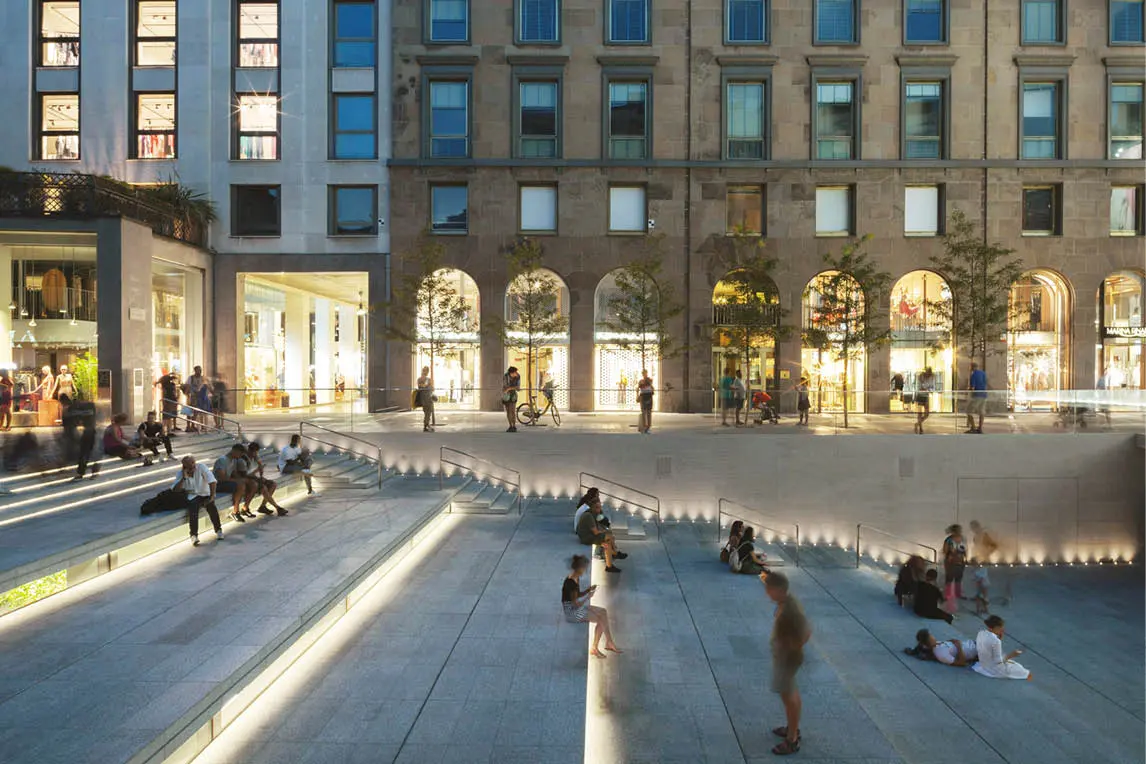 Pedestrian square with lit steps in front of a historic building at dusk