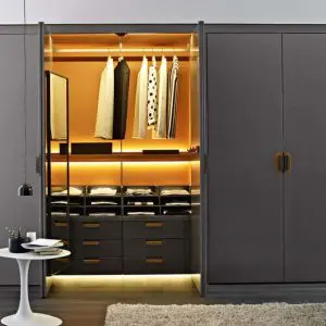 Open wardrobe with amber interior lighting, hanging clothes and drawers