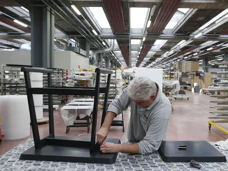 Worker assembling a black wood chair frame in a furniture factory