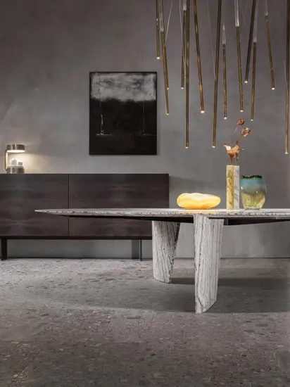 Dining table with a stone base beneath hanging pendant lights and a dark wood sideboard