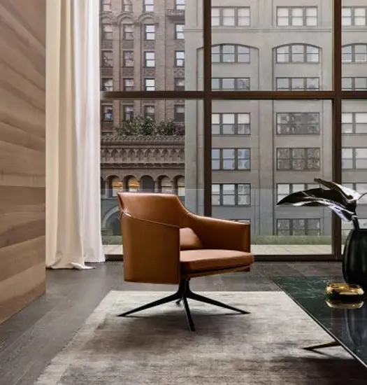 Tan leather lounge chair beside floor-to-ceiling windows overlooking city buildings