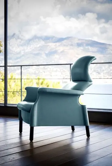 Curved teal lounge chair facing a window view of mountains and the coast