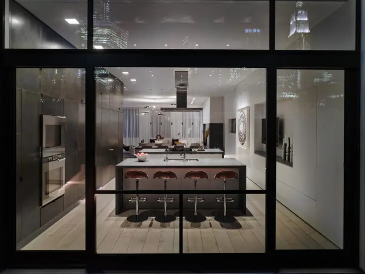 Night view through glass into a kitchen island with bar stools and city skyline reflections