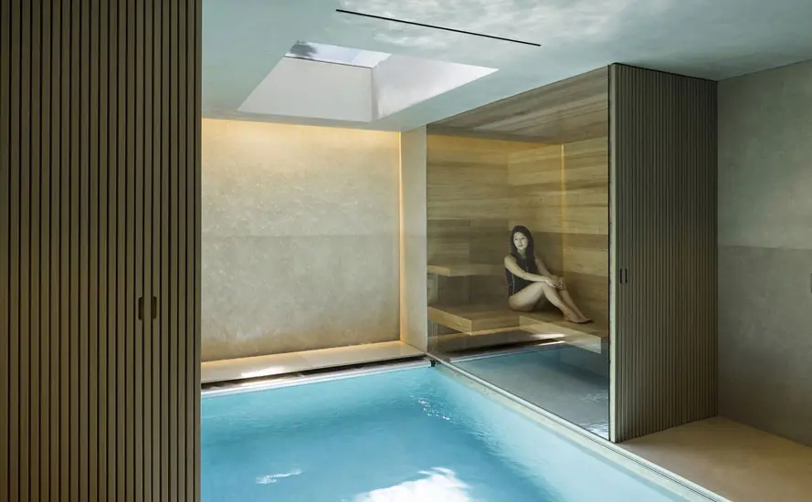 Indoor lap pool with a wood-paneled sauna alcove and a skylight, a woman sitting inside