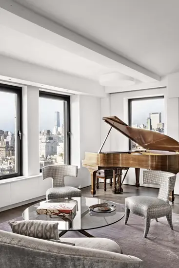 Grand piano in a bright corner room with a city skyline view through the windows