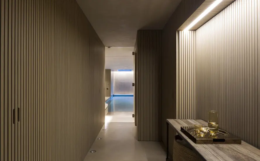 Wood slat hallway leading to a blue-lit indoor pool