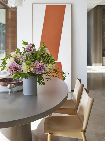 Dining table with a pink and white floral bouquet beside an orange abstract painting