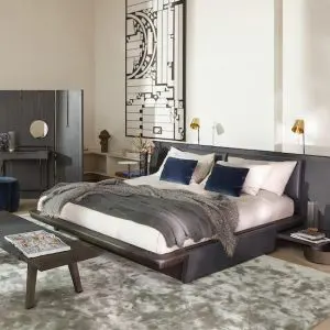 Bedroom with a dark grey upholstered bed, navy and grey pillows and a wooden bench at the foot of the bed
