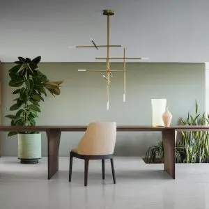 Dining area with a wooden table, beige chair and a linear brass pendant light against a sage green wall