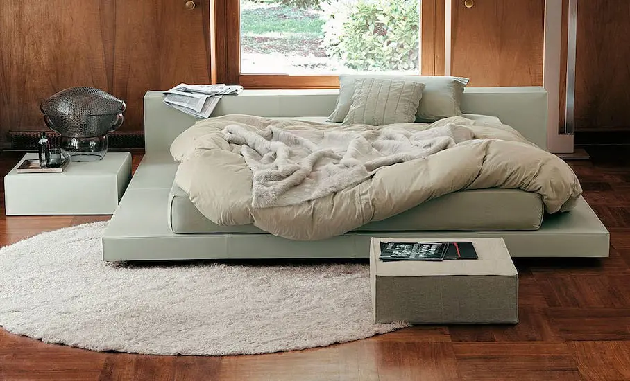 Bedroom with a low sage green upholstered platform bed, rumpled bedding, a shag rug and wood-panelled walls