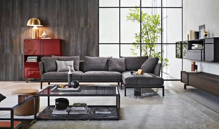 Living room with a grey sectional sofa, red lacquered cabinet and a potted plant by floor-to-ceiling windows