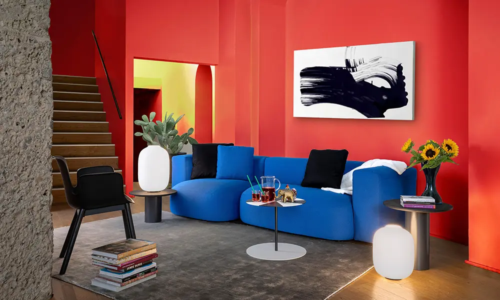 Contemporary living room with red walls, a curved blue sofa, black-and-white abstract painting and a wooden staircase