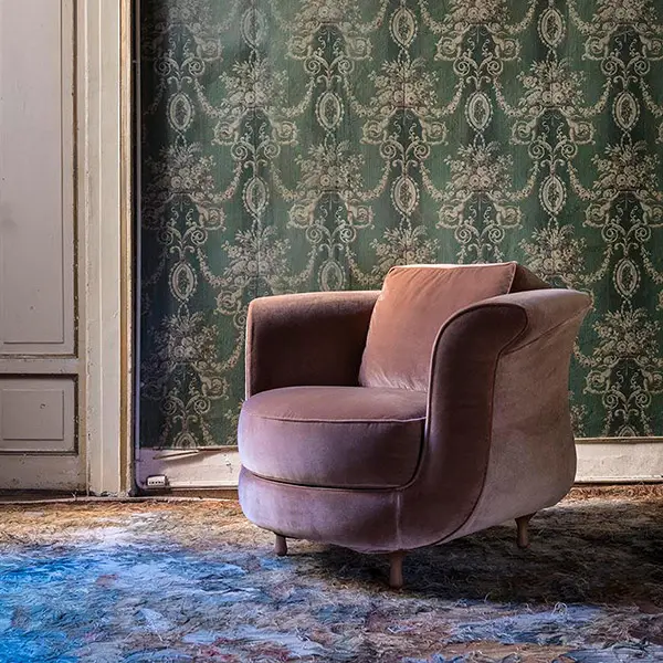 Blush pink velvet Moroso Big Mama armchair against faded green floral wallpaper on a weathered marble floor