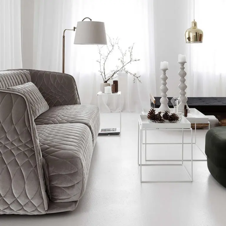 Living room with a grey quilted Redondo sofa by Moroso, brass floor lamp and white side tables with candle holders