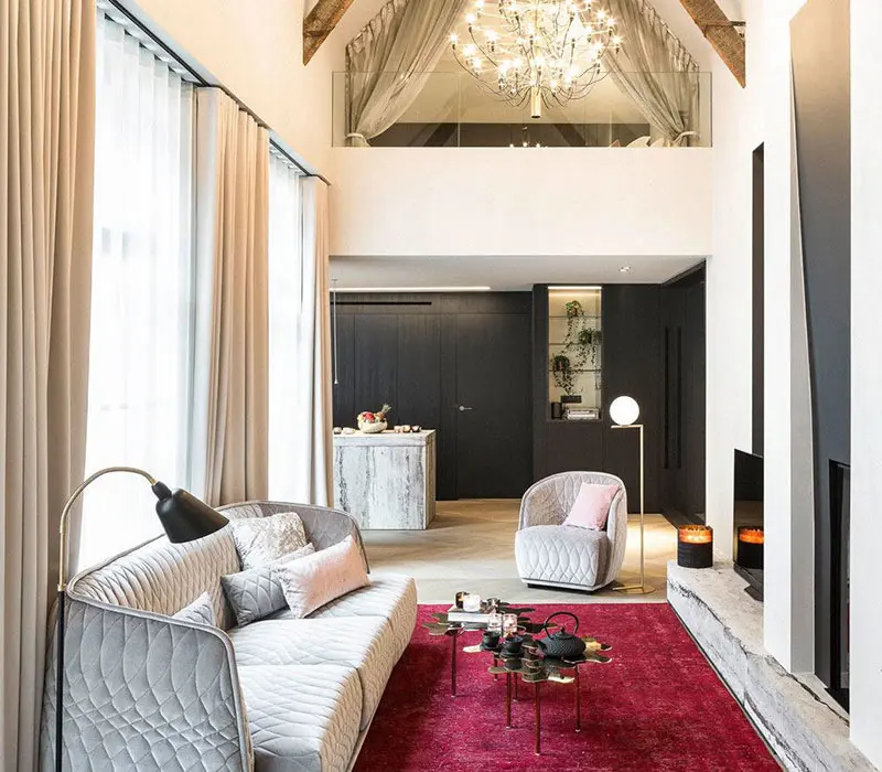 Living room with a grey quilted sofa, deep red rug and a mezzanine gallery under a chandelier
