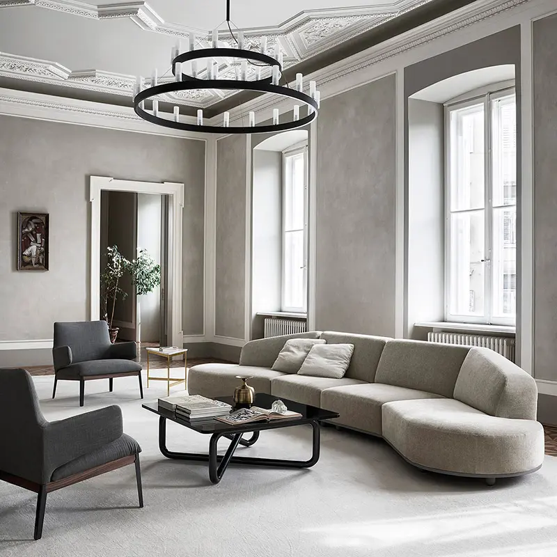 Curved beige sofa in an ornate period living room with a black ring chandelier and tall arched windows