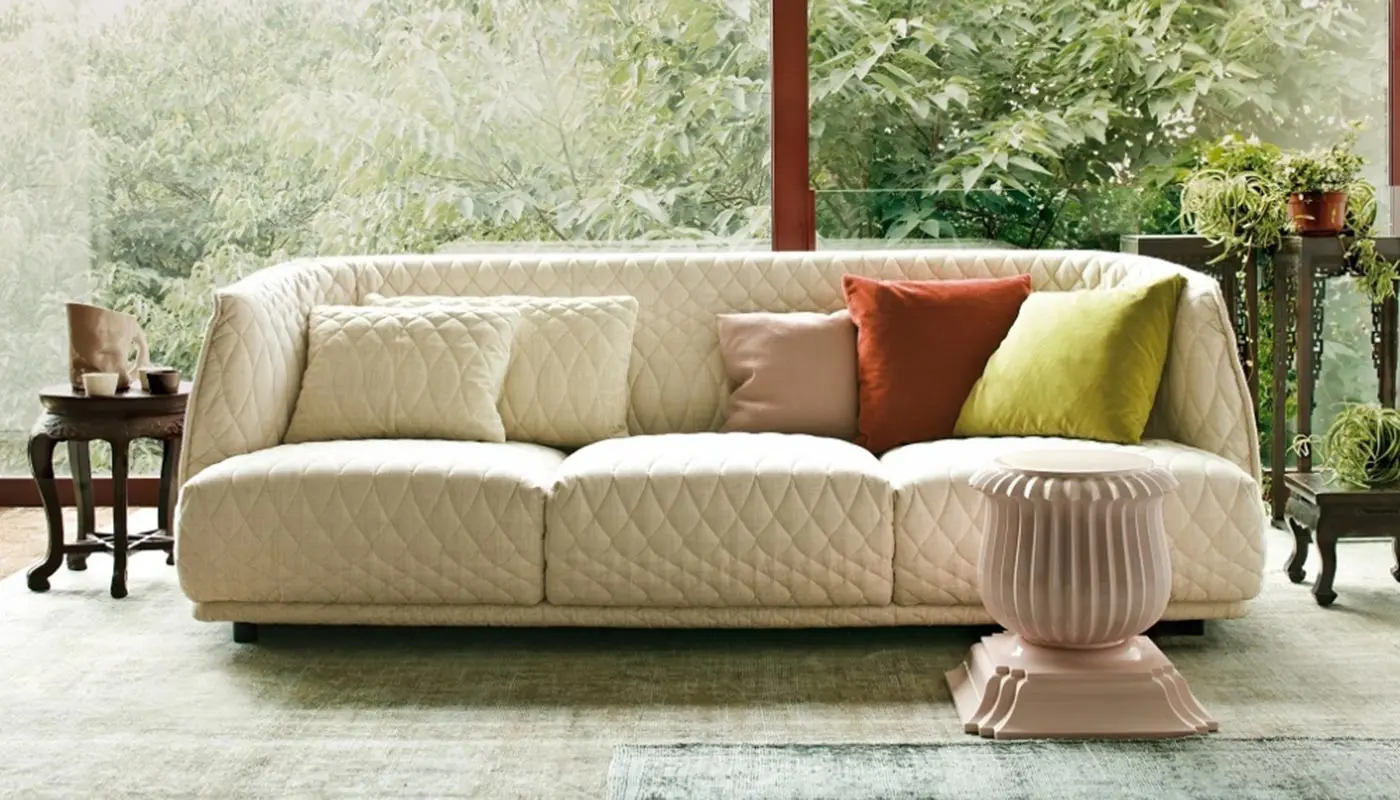 Cream quilted sofa with colourful velvet cushions by floor-to-ceiling windows overlooking greenery