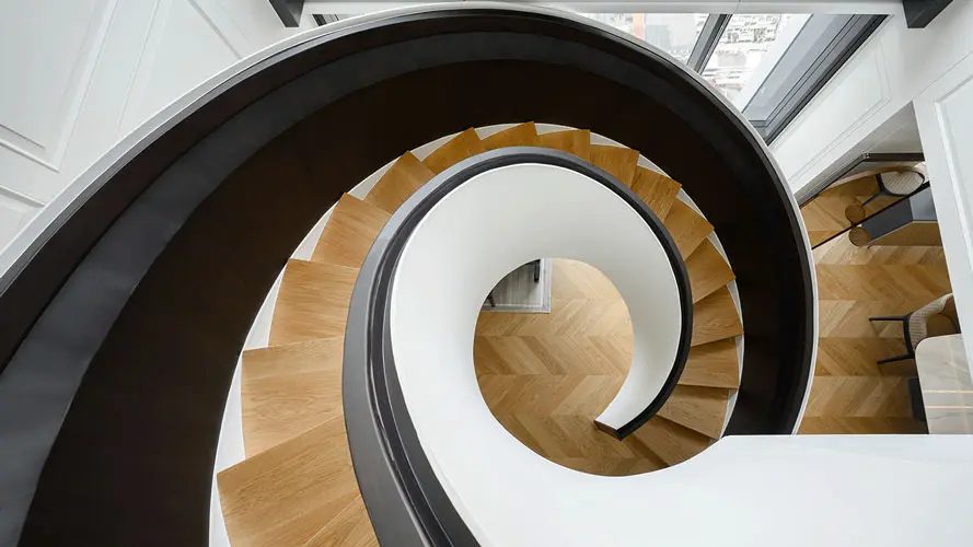 Spiral staircase with dark handrail and wood herringbone treads seen from above