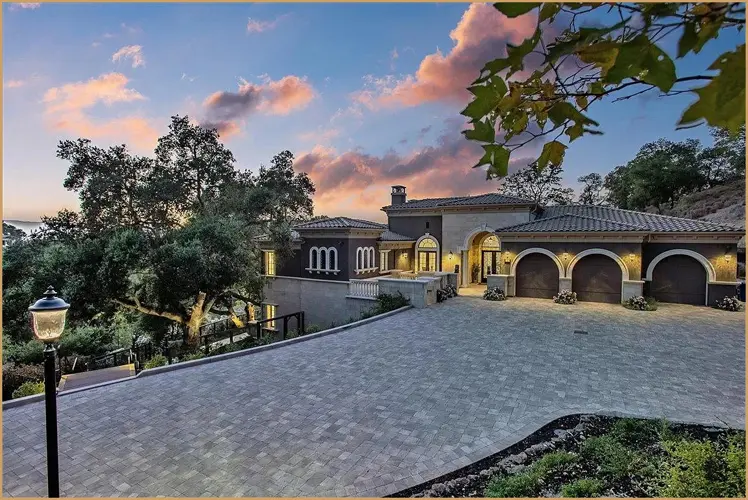 Mediterranean-style hillside villa with a paved driveway at dusk