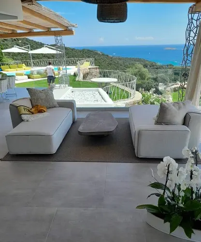 Gray modular outdoor sofas around a stone coffee table facing an infinity pool and sea view